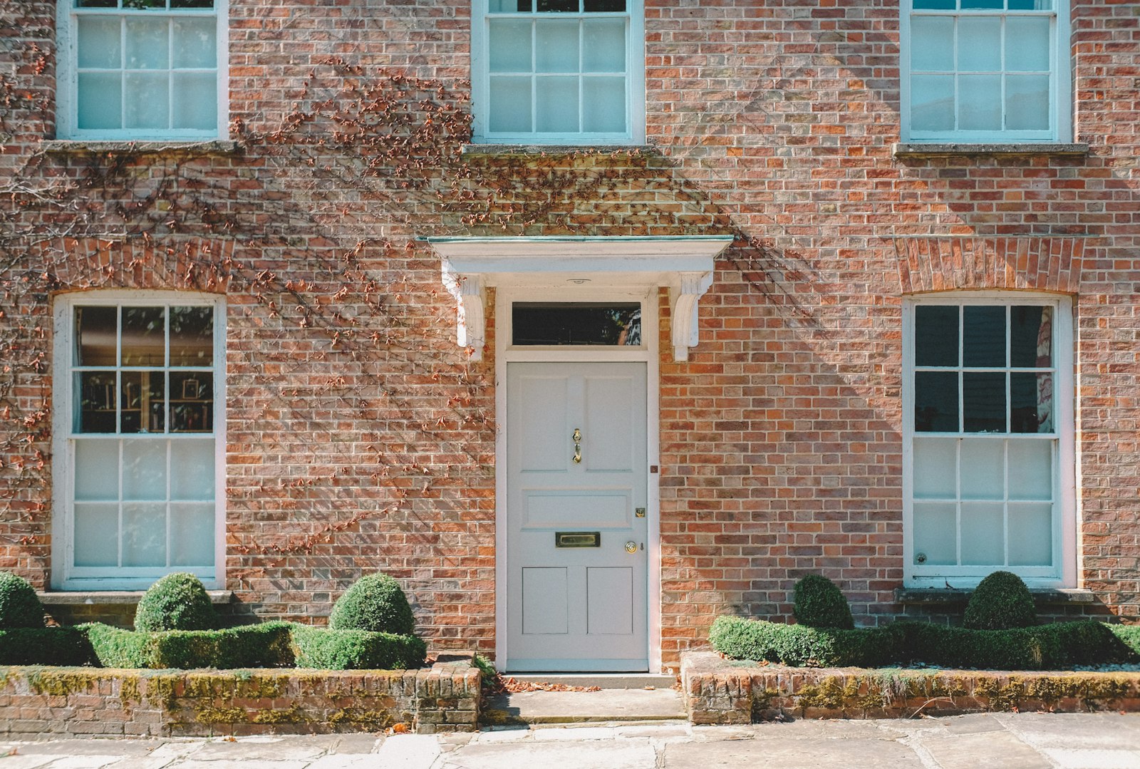 A red brick house with a cream door and ivy across the front